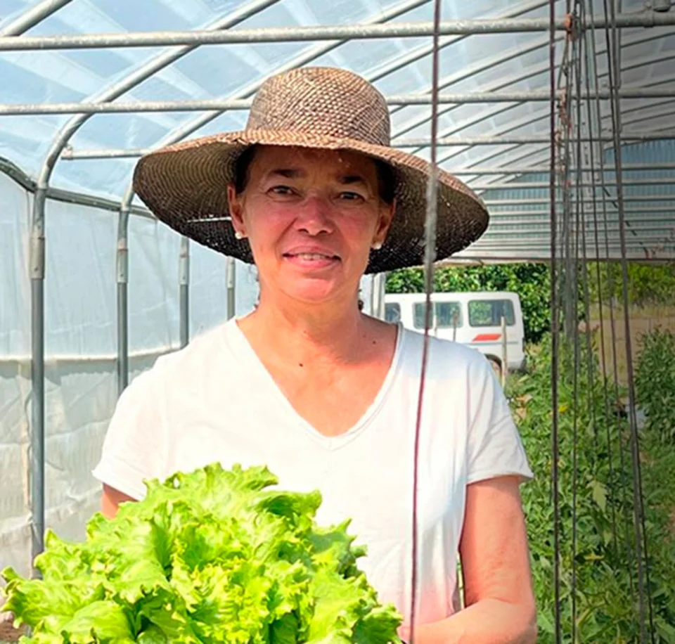 Alicia con un sombrero de paja y una lechuga recién cogida en el huerto